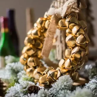 طوق أجراس ذهبي شتوي مزين بشريط خيش موضوع وسط زينة شتوية من أغصان الصنوبر والثلج الصناعي.