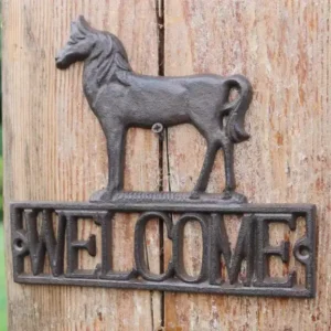 لوحة حصان حديدية ترحيبية باللون الأسود المعدني المعتق تحمل كلمة WELCOME مثبتة بمسامير على سطح خشبي طبيعي.