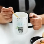 كوب قهوة سيراميك أبيض للمكتب مع غطاء أسود ورسمة نبتة