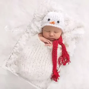 طقم تصوير مواليد كروشيه ثيم رجل ثلج أبيض يظهر به طفل نائم يرتدي قبعة ووشاح أحمر داخل سرير تصوير ناعم