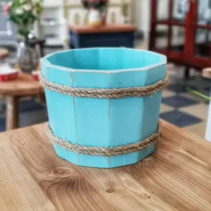 دلو خشبي لتصوير المواليد باللون السماوي المعتق محاط بحبال خيش طبيعية موضوع على طاولة خشبية في استوديو تصوير