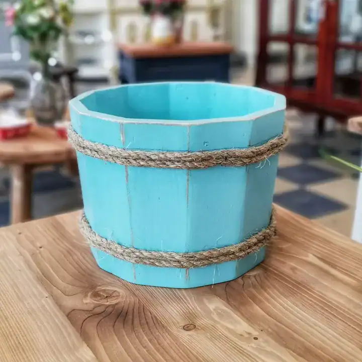 دلو خشبي لتصوير المواليد باللون السماوي المعتق محاط بحبال خيش طبيعية موضوع على طاولة خشبية في استوديو تصوير