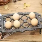 حامل بيض معدني مستطيل باللون البرونزي العتيق يضم 8 بيضات موضوع على طاولة خشبية بتصميم ريفي كلاسيكي