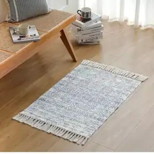 دواسة قماشية مودرن باللون الرمادي المزرق مع أهداب جانبية موضوعة في زاوية استرخاء عصرية بجانب مقعد خشبي وكتب