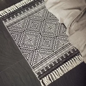 دعاسة باب خارجي قماشية بنقوش هندسية بالأبيض والأسود مع أهداب جانبية موضوعة في مدخل عصري بجانب السرير