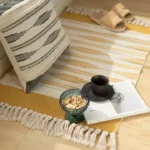 دعاسة مدخل قماشية مخططة باللون الأصفر الخردلي والأبيض مع أهداب جانبية موضوعة في زاوية استرخاء عصرية مع مخدة ديكور