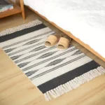 سجاد باب مخطط باللون البيج والأسود من القطن مع أهداب جانبية موضوعة في مدخل غرفة نوم عصرية بجانب السرير