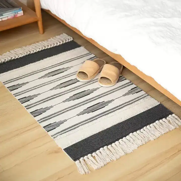 سجاد باب مخطط باللون البيج والأسود من القطن مع أهداب جانبية موضوعة في مدخل غرفة نوم عصرية بجانب السرير