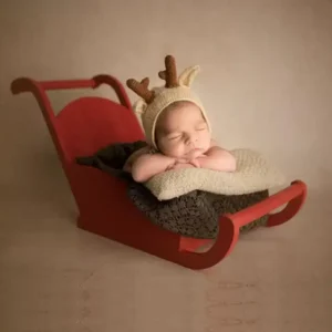 عربة ثلجية خشبية باللون الأحمر بتصميم كلاسيكي تستخدم كوعاء تصوير لحديثي الولادة في جلسات التصوير الشتوية الفاخرة