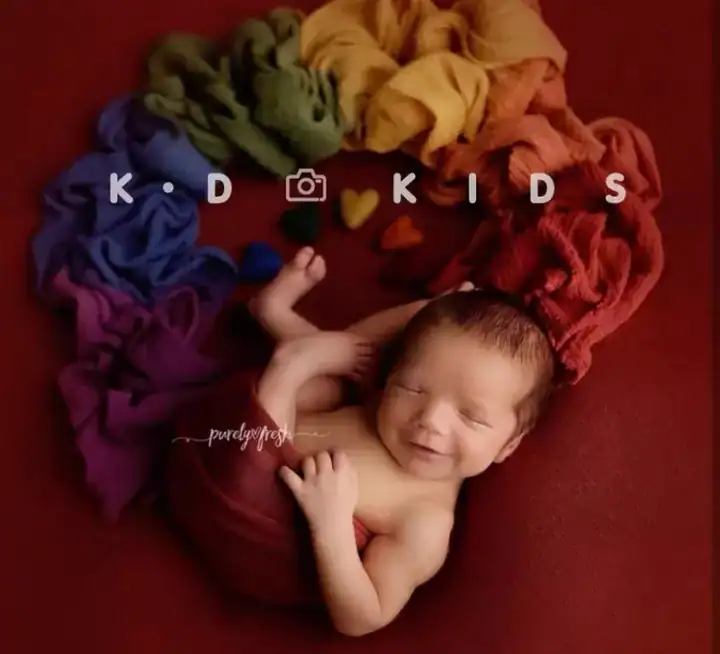 طفل مولود ملفوف بقماش ستريتش احمر ومحاط بلفات ملونة تشكل قوس قزح