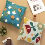 مجموعة كوشن نباتي قطنية مطرزة يدوياً بأشكال أزهار ملونة بالبرتقالي والأبيض فوق خلفية زرقاء وسماوية لتزيين الكنب