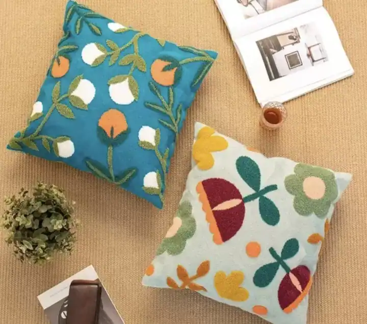 مجموعة كوشن نباتي قطنية مطرزة يدوياً بأشكال أزهار ملونة بالبرتقالي والأبيض فوق خلفية زرقاء وسماوية لتزيين الكنب