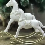 حصان هزاز ديكور صغير الحجم مصنوع من الريزن الأبيض مع سرج وقاعدة منحنية باللون الذهبي بتصميم كلاسيكي فاخر.